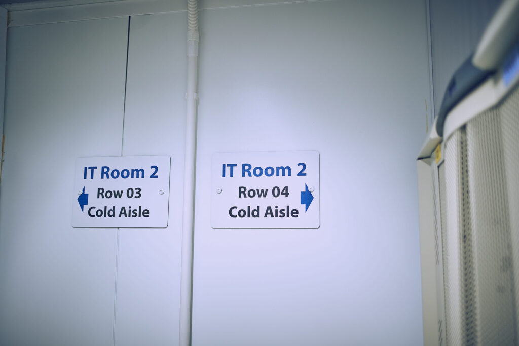 image of the end of the data centre room showing a sign with arrows to further aisles